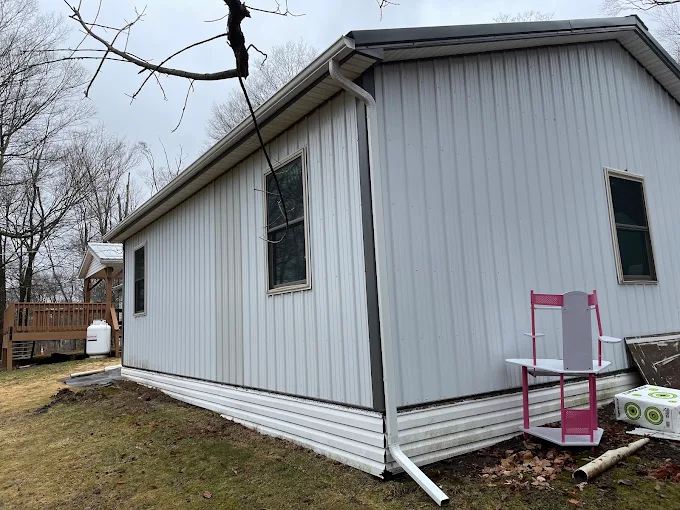 White metal-sided building with a new white gutter and downspout along the eave