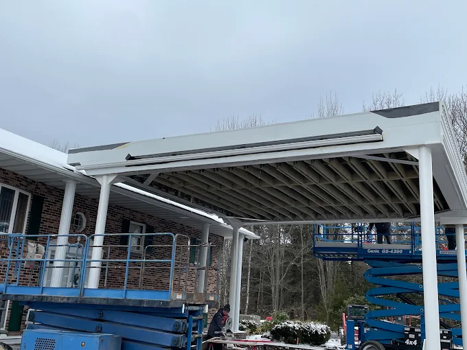 Crew on lifts installing a new commercial porch roof structure over a brick building entrance