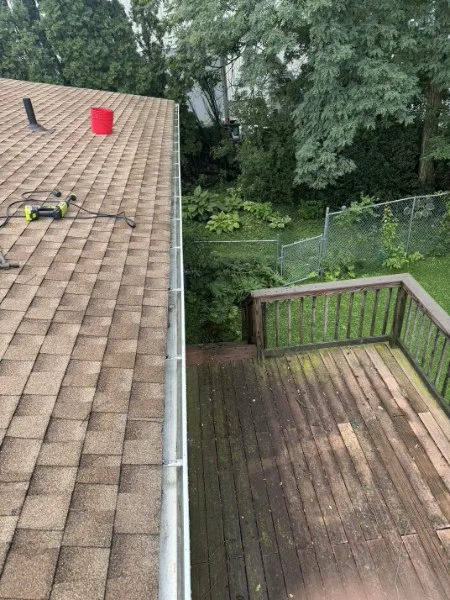 Clear, freshly cleaned white gutter running along a shingle roof above a wood deck in Moosic, PA