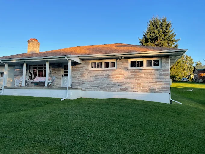 Stone ranch home with white seamless gutters and downspouts at golden hour