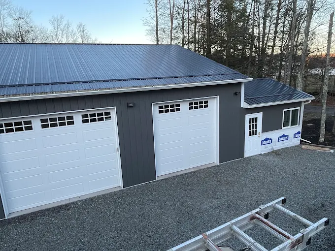 Detached garage with a dark standing seam metal roof and white overhead doors