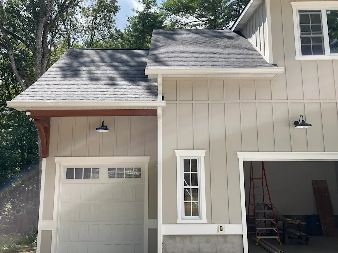 Board-and-batten garage with a new shingle roof, white fascia and seamless gutter