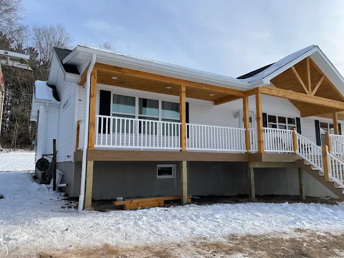 Newly built covered porch with cedar posts, white railing and seamless white gutter on a winter job site