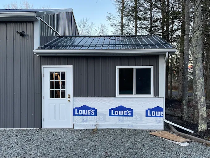 Dark board-and-batten outbuilding with a black metal roof and white downspout