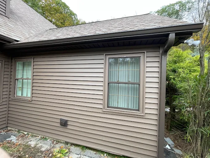 Brown clapboard home with a dark bronze gutter run and matching downspout